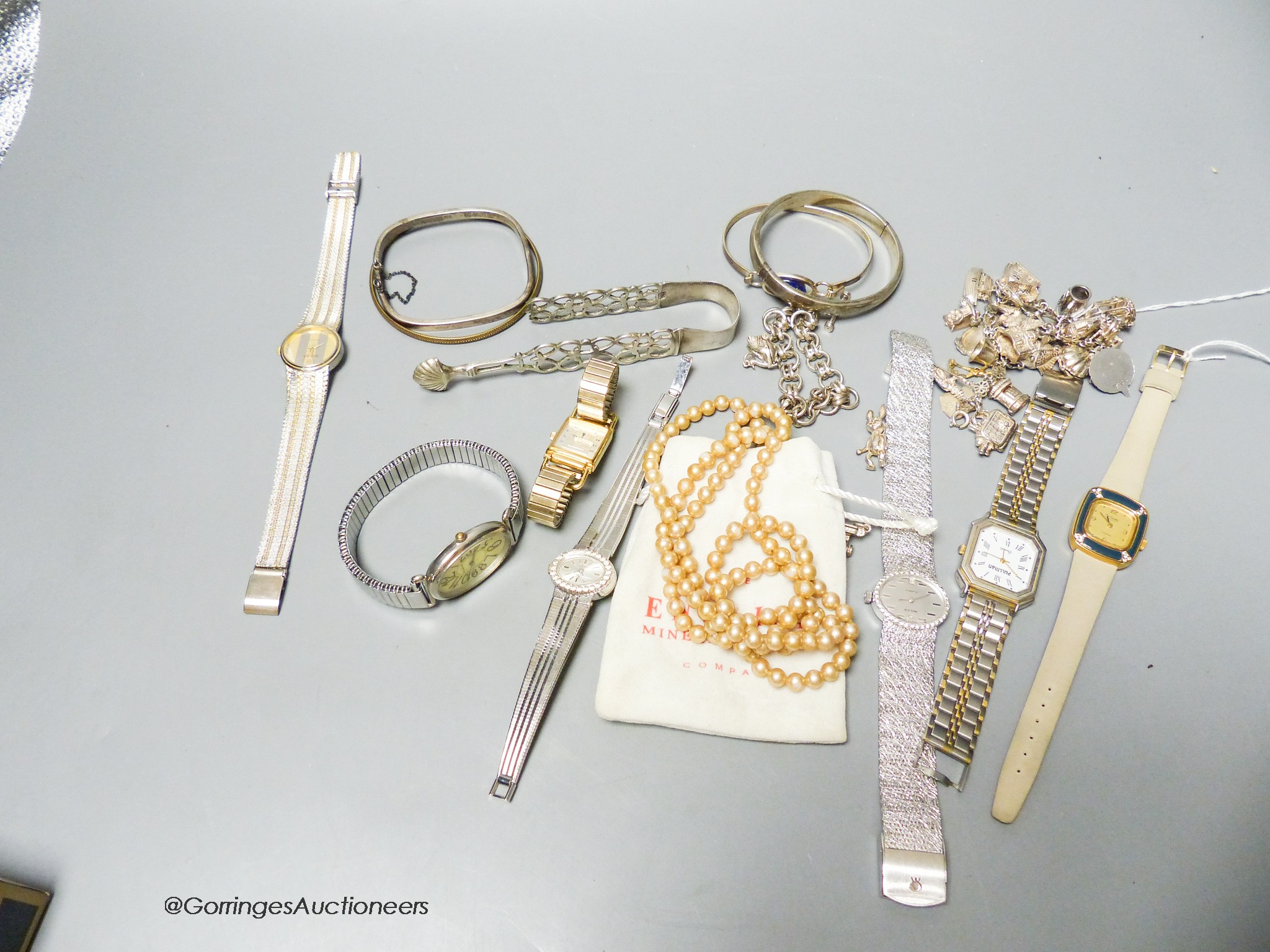 A white metal charm bracelet, five additional charms, a silver chain bracelet, four various bangles, a pair of silver sugar tongs (a.f.) and seven ladys' fashion wristwatches